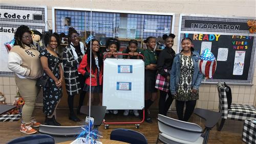 A group of African American students behind a vote here sign.